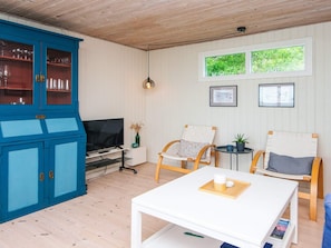 A room with a blue cabinet, a TV, two chairs, a small table, and a window with greenery outside.