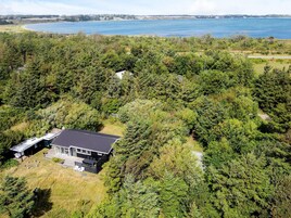 A single-story house surrounded by dense forest, with a view of a large body of water in the background.