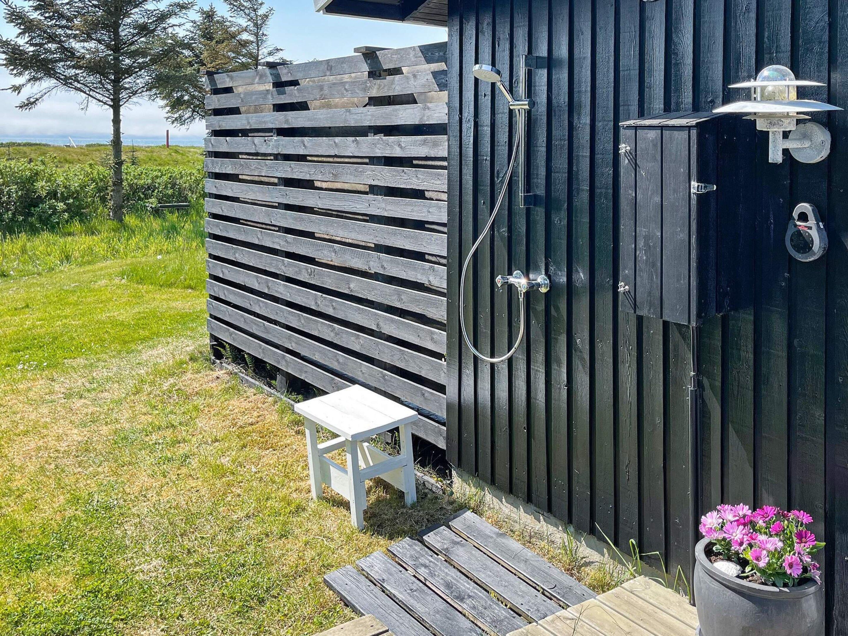 A wooden outdoor shower area with a white bench and a potted plant.