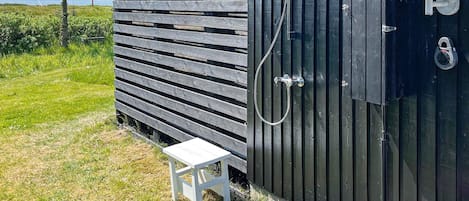 A wooden outdoor shower area with a white bench and a potted plant.