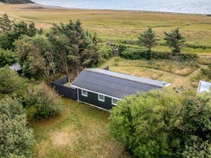 A house with a sloped roof, surrounded by dense vegetation and a beach in the background. - 6 Person Holiday Home in Thyholm (Thyholm)