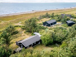 Una propiedad costera con varias construcciones, incluyendo una casa grande con terraza y una estructura más pequeña, rodeada de vegetación densa y una playa al fondo.