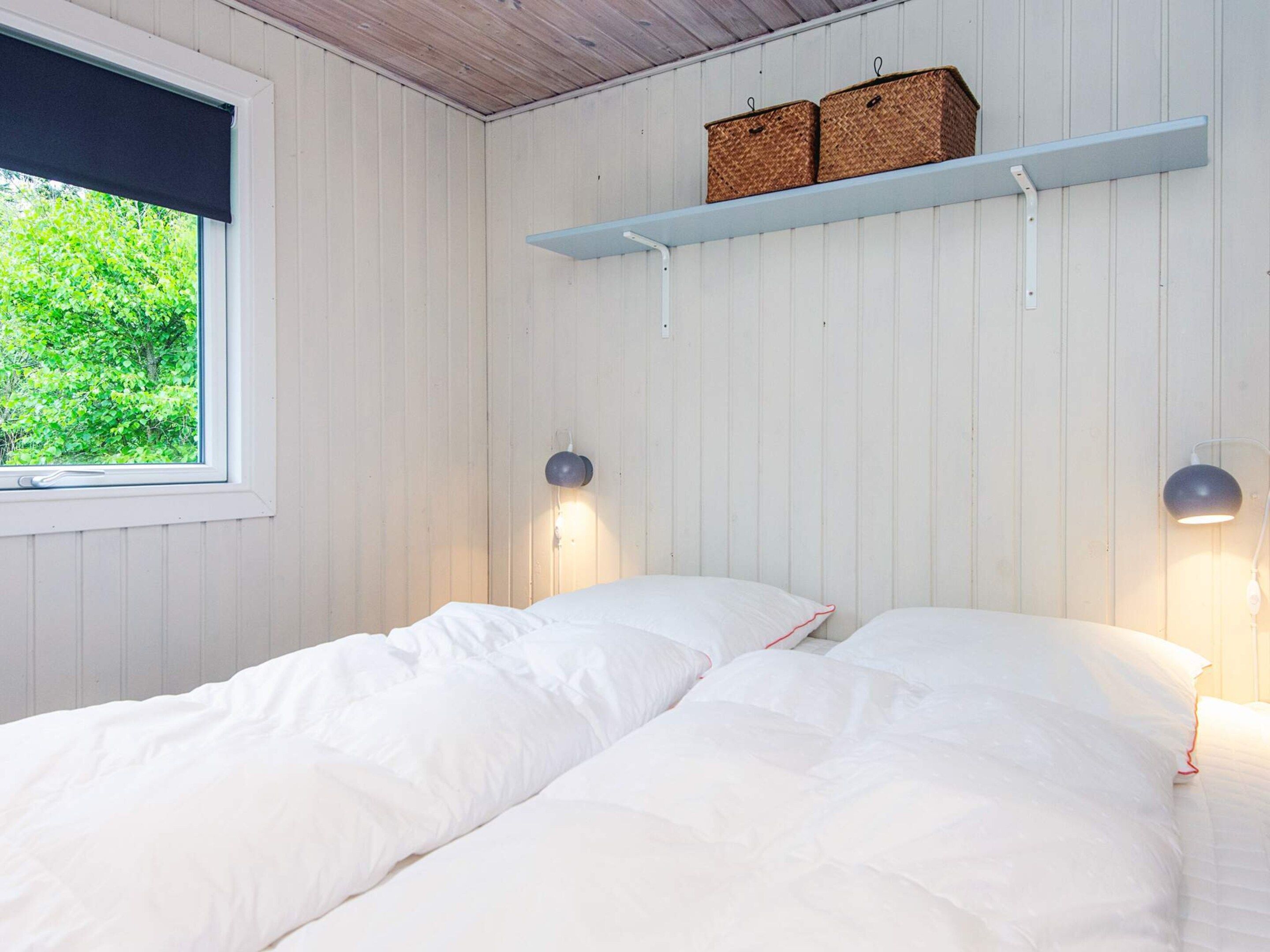 Une chambre avec deux lits, une fenêtre et deux lampes fixées au mur.