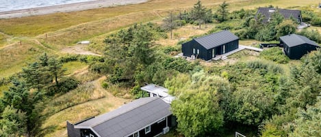 Una propiedad costera con varias construcciones, incluyendo una casa grande con porche cubierto y una estructura más pequeña, rodeada de vegetación densa y una playa al fondo.