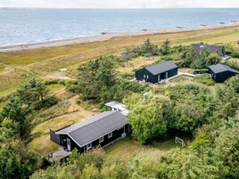 Una propiedad costera con varias construcciones, incluyendo una casa grande con porche cubierto y una estructura más pequeña, rodeada de vegetación densa y una playa al fondo.