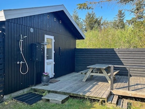 A wooden deck with a picnic table, a shower area with a door, and a small potted plant.