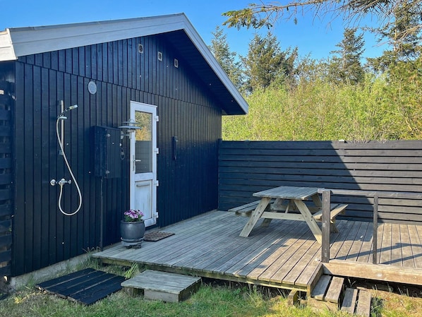 A wooden deck with a picnic table, a shower area with a door, and a small potted plant.