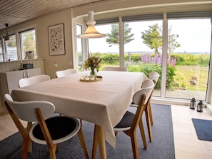 A dining area with a table set for four, chairs, a vase with flowers, and a view of a garden through large windows.