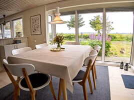 A dining area with a table set for four, chairs, a vase with flowers, and a view of a garden through large windows.
