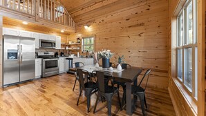 A wooden cabin interior with a kitchen, dining area, and a loft bedroom.