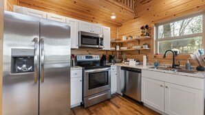 A modern kitchen with stainless steel appliances, wooden ceiling, and a large window providing natural light. - Nature Retreat Near Buffalo River w/ Hot Tub (Jasper)