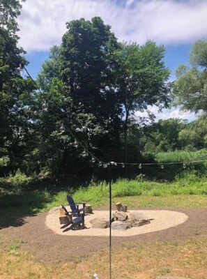 Relax by the fire pit in a serene natural setting, surrounded by trees and grass.
