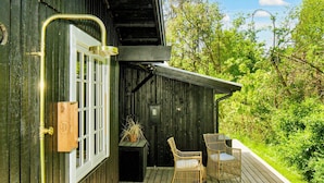 A wooden deck with wicker chairs and a small table, a window with a white frame, and a door with a brass handle. - 8 Person Holiday Home in Vejby (Vejby)