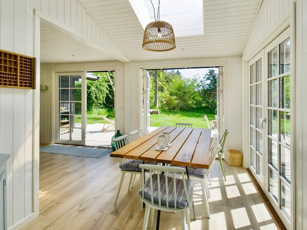 Enjoy meals at the large dining table surrounded by comfortable chairs, with a view of the lush garden through large windows.