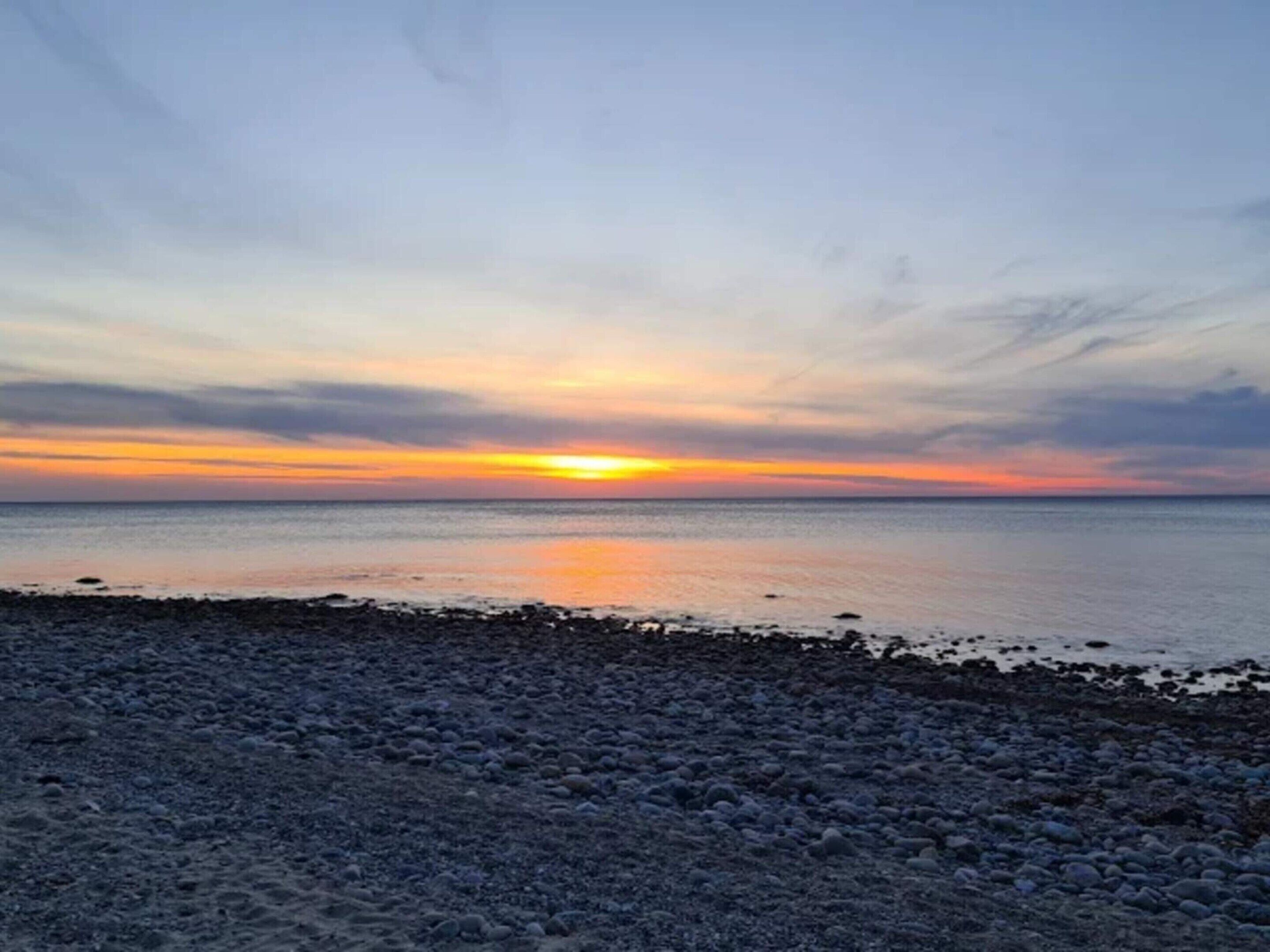 Un atardecer sobre una playa rocosa con agua tranquila.