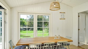 A dining area with a wooden table and white chairs, large windows with a view of greenery, and a hanging light fixture. - 8 Person Holiday Home in Vejby (Vejby)