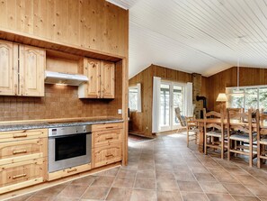A kitchen with wooden cabinets, a stainless steel oven, and a dining area with a table and chairs.