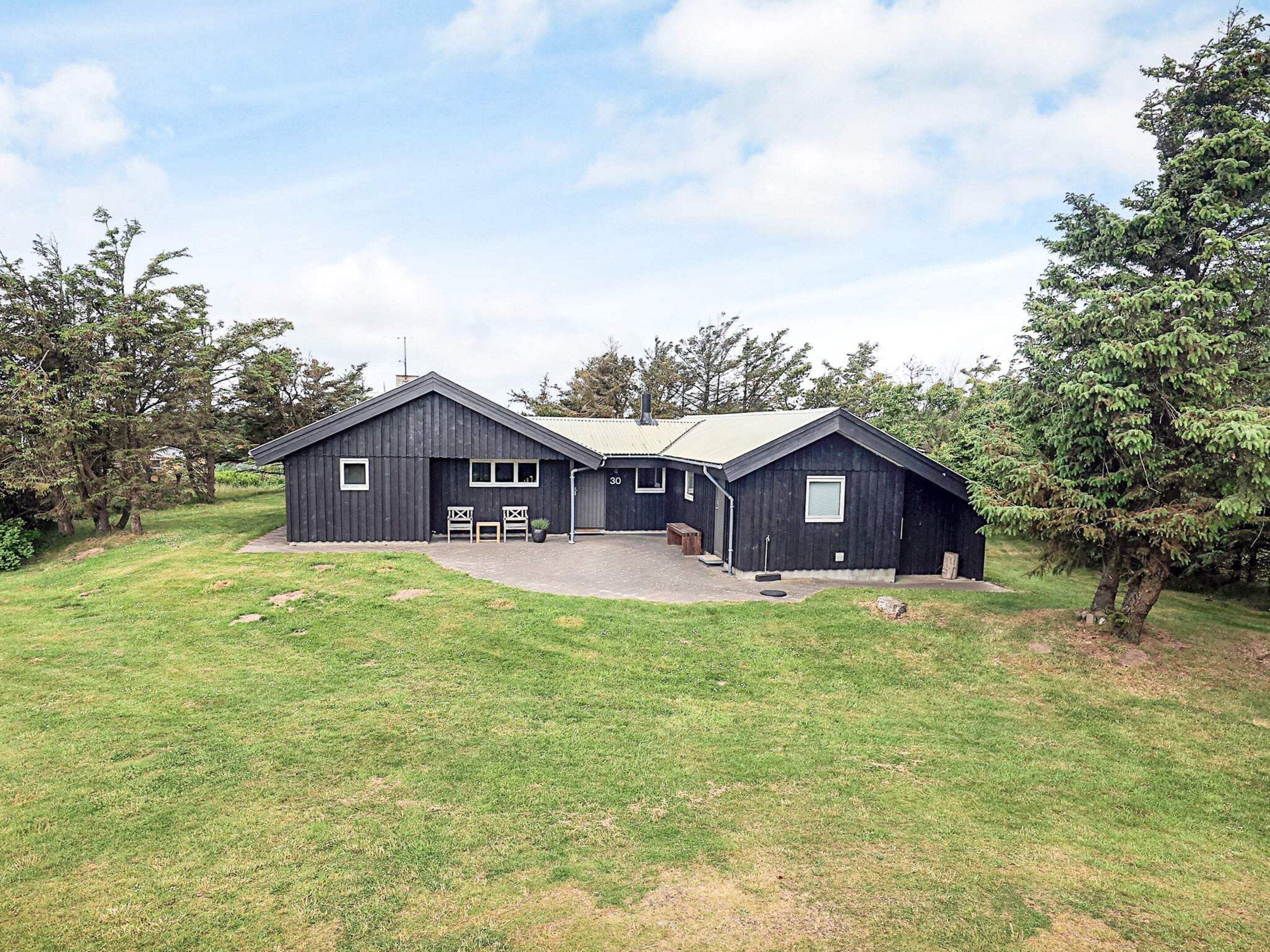 A two-story black wooden building with a covered porch and a small outdoor seating area.