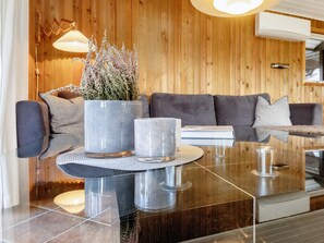 A modern living room with a wooden wall, a grey sofa, a glass coffee table, and a potted plant. - 8 Person Holiday Home in Lokken (Lokken)