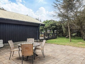An outdoor patio with a table and four wicker chairs, a covered area with a metal roof, and a wooden deck with railings.
