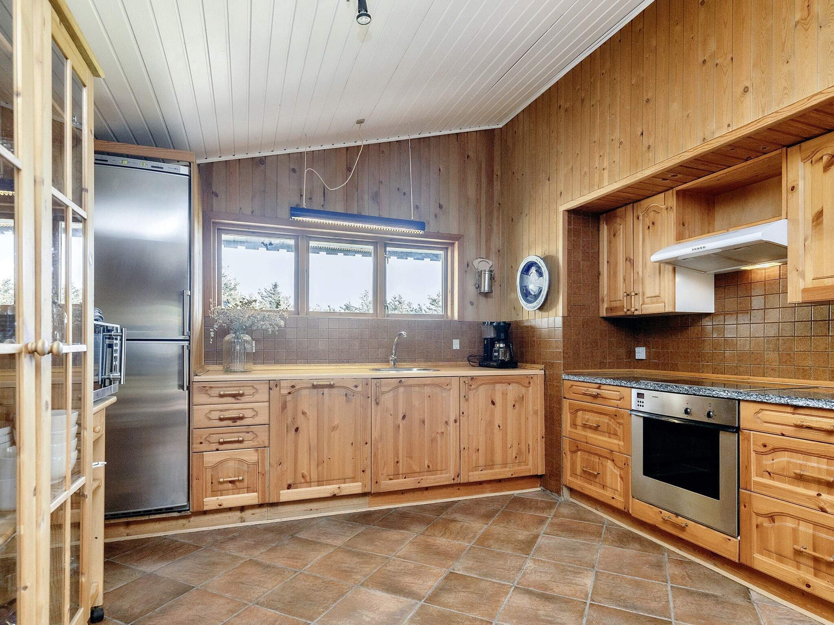 A kitchen with wooden cabinets, a stainless steel refrigerator, a built-in oven, and a window with a view.
