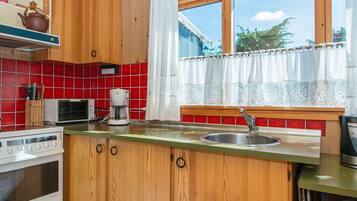 Una cocina con armarios de madera, microondas, cafetera y ventana con cortinas.
