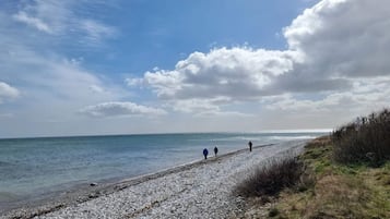 A pebbled beach path leading to the sea with a clear sky and a few clouds.