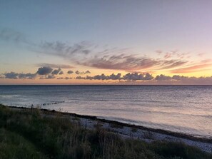 Une vue sur le coucher de soleil sur la côte, avec une mer calme et un premier plan verdoyant.