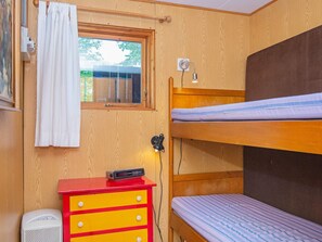 Un lit superposé avec une fenêtre, une commode rouge avec des tiroirs, un radiateur et une lampe fixée au mur.