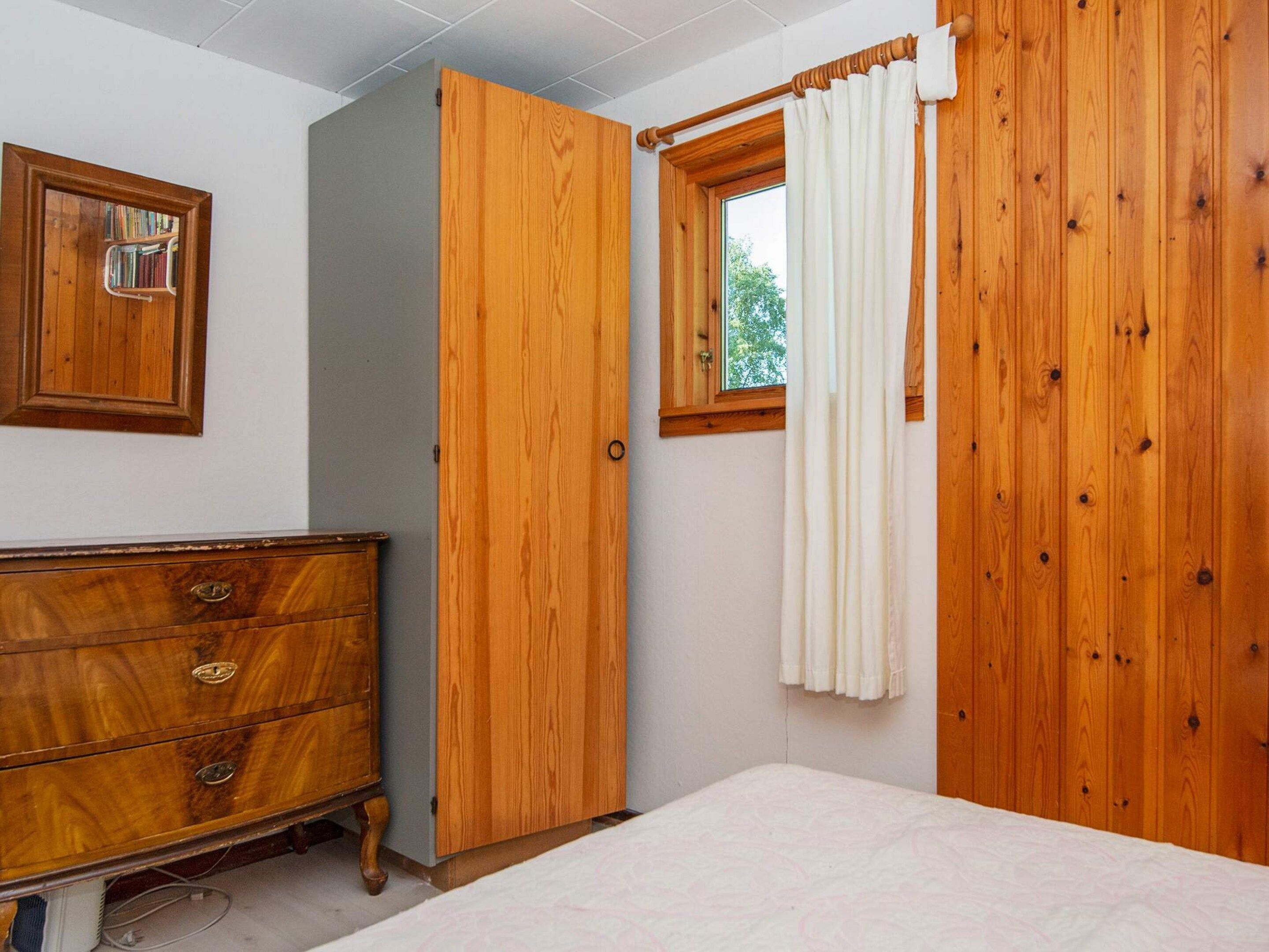 A bedroom with a wooden wardrobe, a bedside table, and a window with curtains.