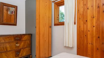 A bedroom with a wooden wardrobe, a bedside table, and a window with curtains.