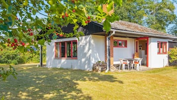 A small house with a white exterior, red-framed windows, and a visible outdoor seating area.