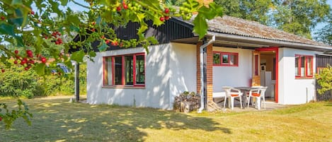 A small house with a white exterior, red-framed windows, and a visible outdoor seating area.