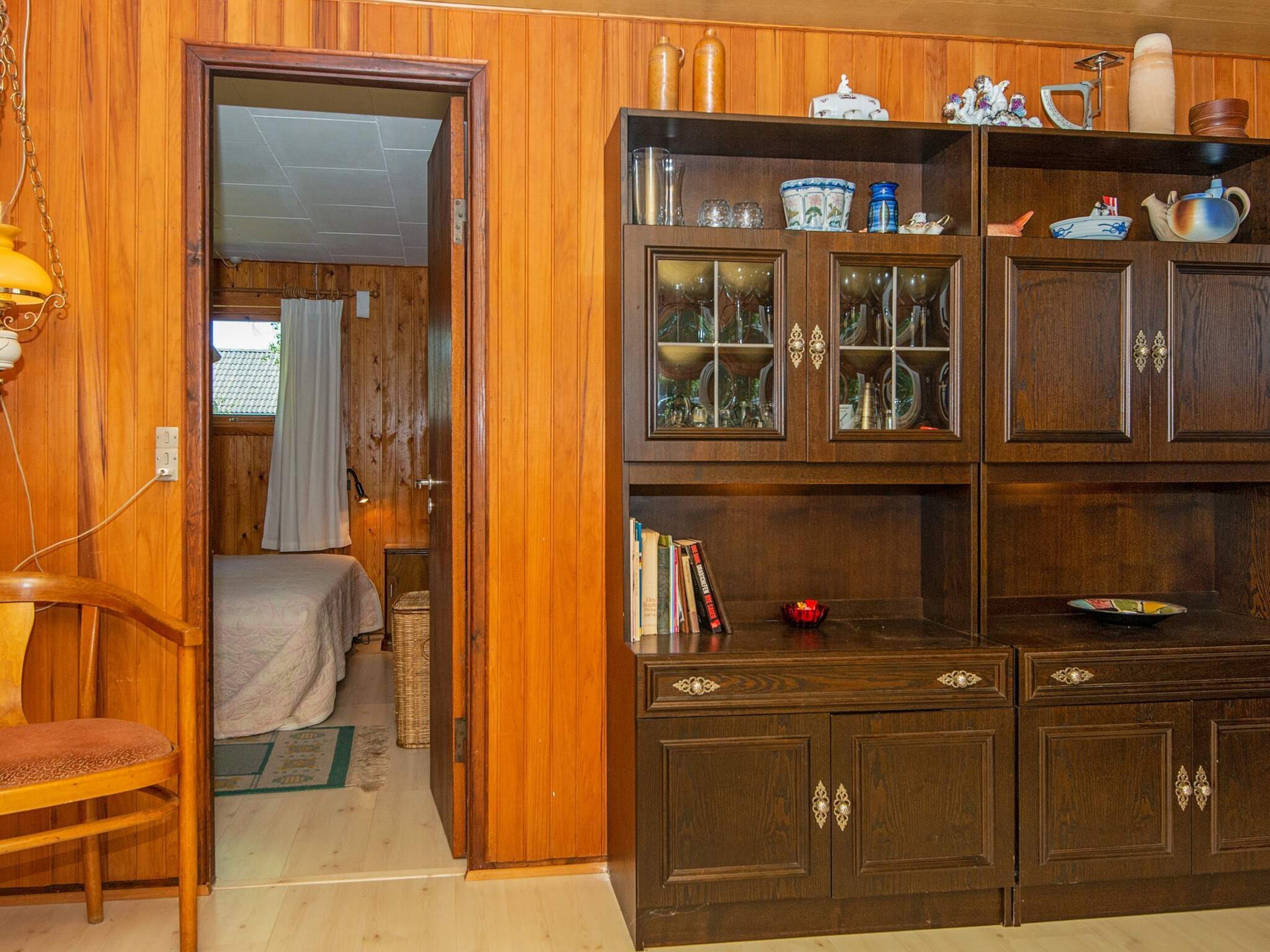 A wooden-paneled room with a bed, a bookshelf, and a cabinet with glass doors.