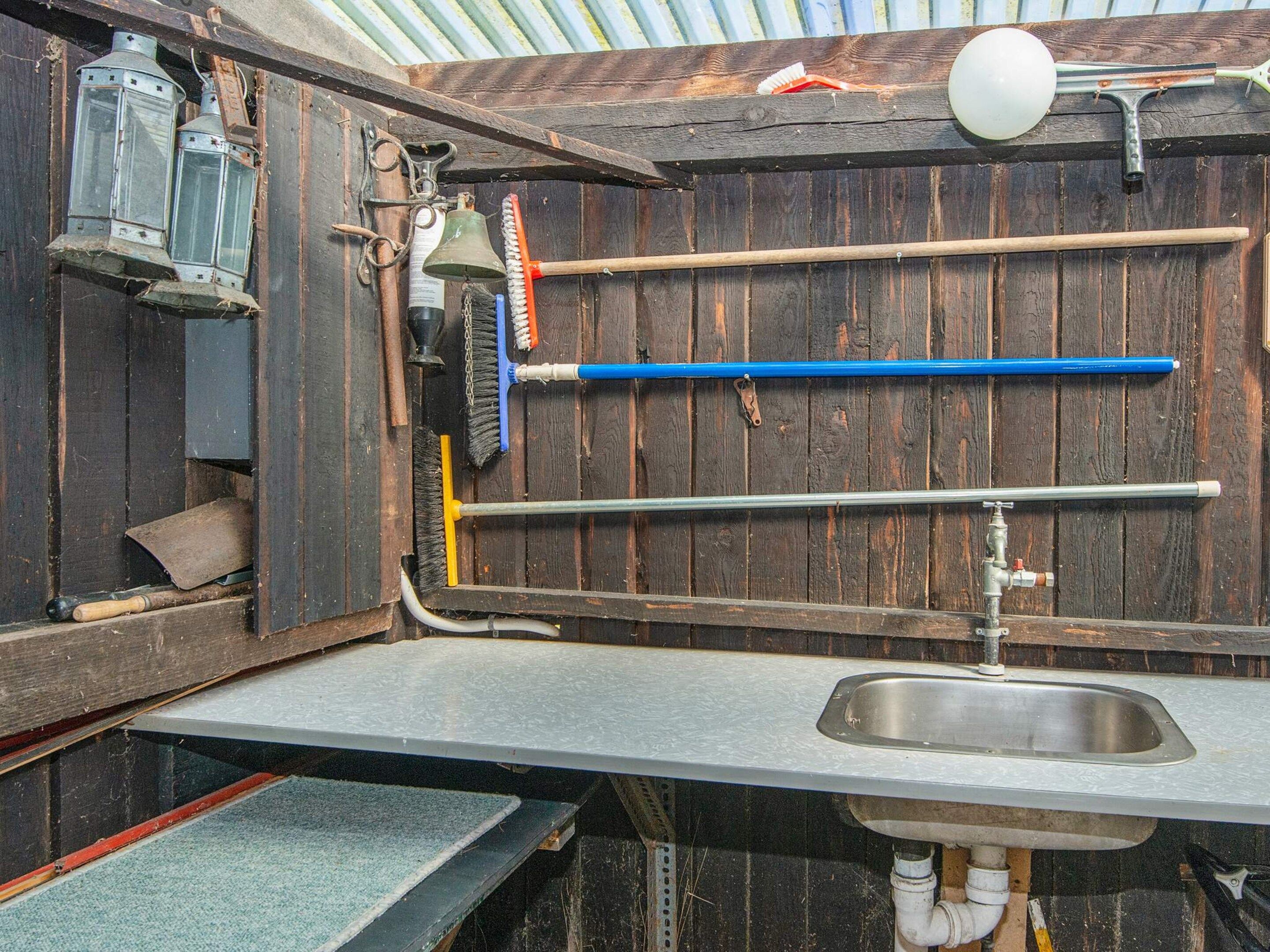 Un baño rústico con pared de madera, un lavamanos de metal y diversos utensilios de limpieza.