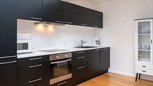 Eine moderne Küche mit dunklen Schränken, einer weißen Arbeitsplatte, einem eingebauten Ofen, einer Mikrowelle und einer Kaffeemaschine.