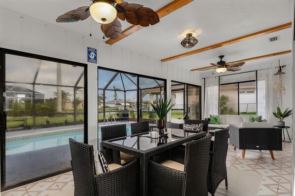 A modern indoor space with a pool view, wicker furniture, ceiling fans, and large windows. - Canal View! Walking distance to Marina Village Fully Renovated (Cape Coral)
