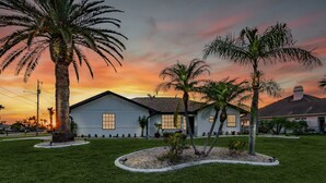 A house with a well-maintained lawn, palm trees, and a sunset sky. - Canal View! Walking distance to Marina Village Fully Renovated (Cape Coral)
