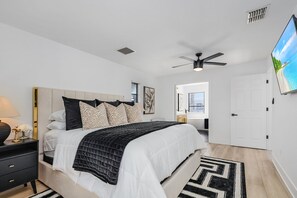 A bedroom with a bed, a nightstand, a ceiling fan, and a TV on the wall. - Canal View! Walking distance to Marina Village Fully Renovated (Cape Coral)