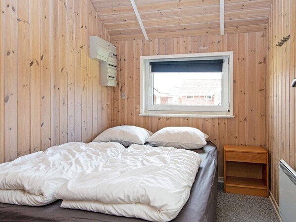 A wooden-paneled room with a bed, a window, and a heater.