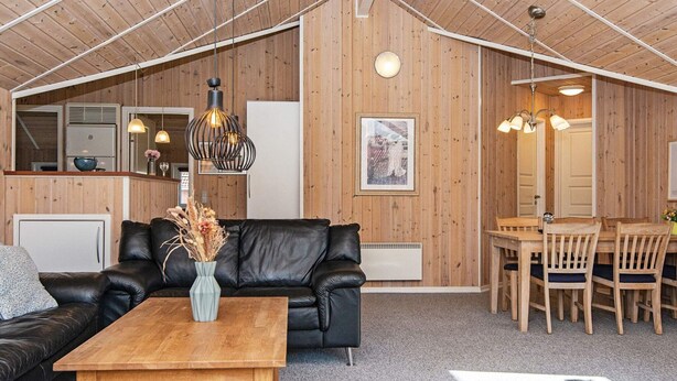 A cozy living room with a black leather sofa, a wooden coffee table, and a dining area with wooden chairs and a table. - 8 Person Holiday Home in Oksbol (Oksbol)