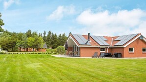 A house with a sloped roof, solar panels, a patio with outdoor furniture, and a well-maintained lawn. - 8 Person Holiday Home in Oksbol (Oksbol)