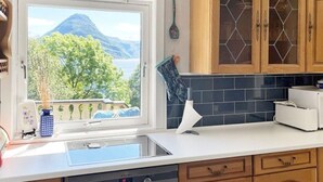 Een keuken met uitzicht op een berg en bomen, houten keukenkastjes, een wit aanrechtblad en een ingebouwde oven.