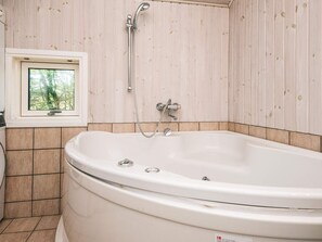 Een badkamer met een vrijstaand bad, een raam met uitzicht op bomen en een houten wand.