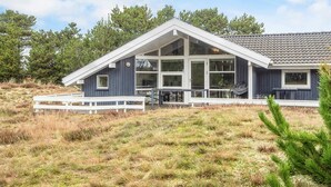 Una casa moderna con un amplio ventanal, un porche blanco y un paisaje cubierto de césped.