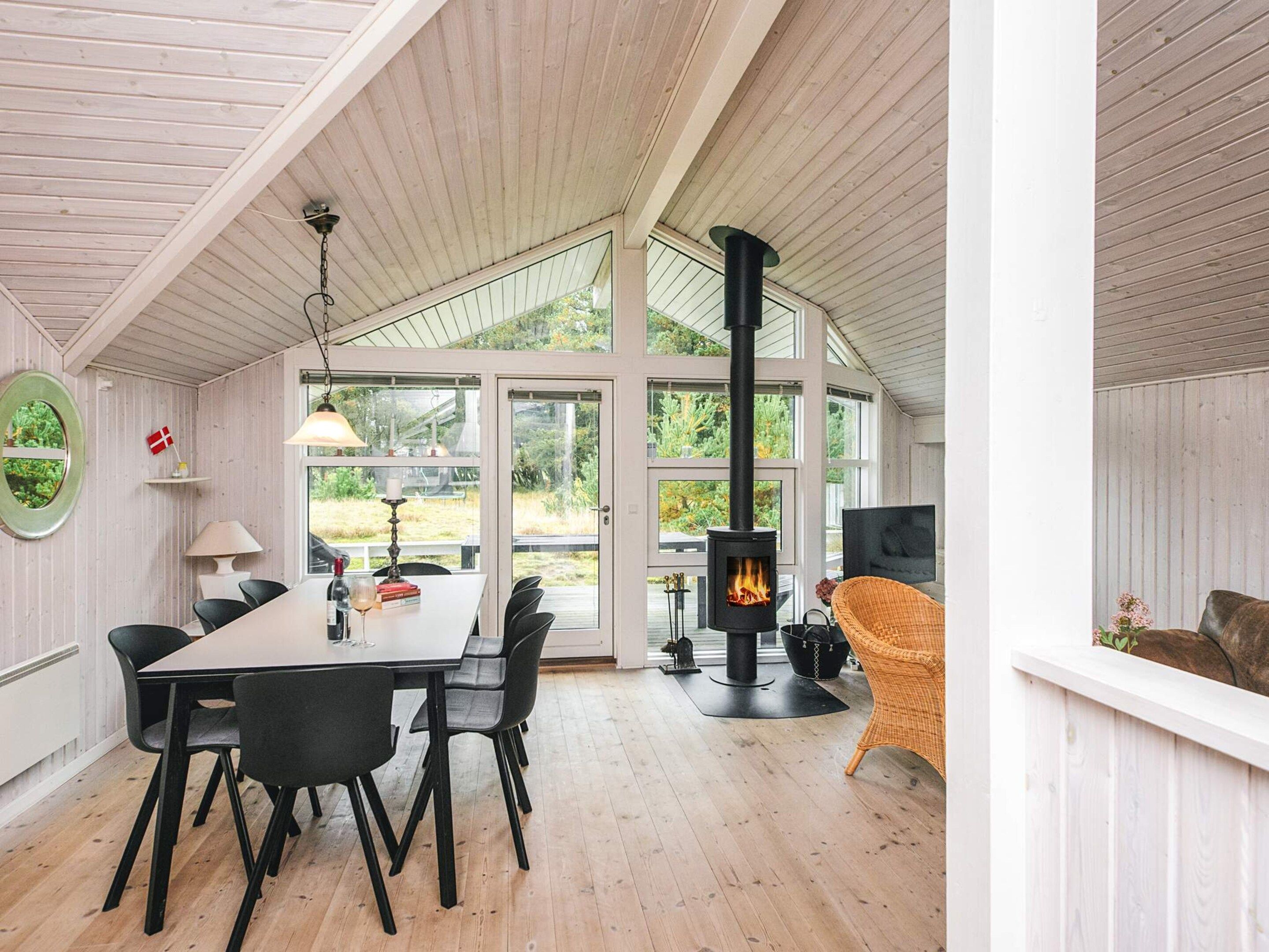 Une pièce chaleureuse avec une table à manger, des chaises, une cheminée et de grandes fenêtres.