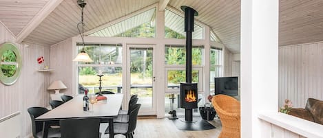 A cozy room with a dining table, chairs, a fireplace, and large windows.
