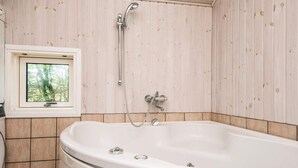 Un baño con una bañera independiente, una ventana que da a árboles y paneles de madera en las paredes.