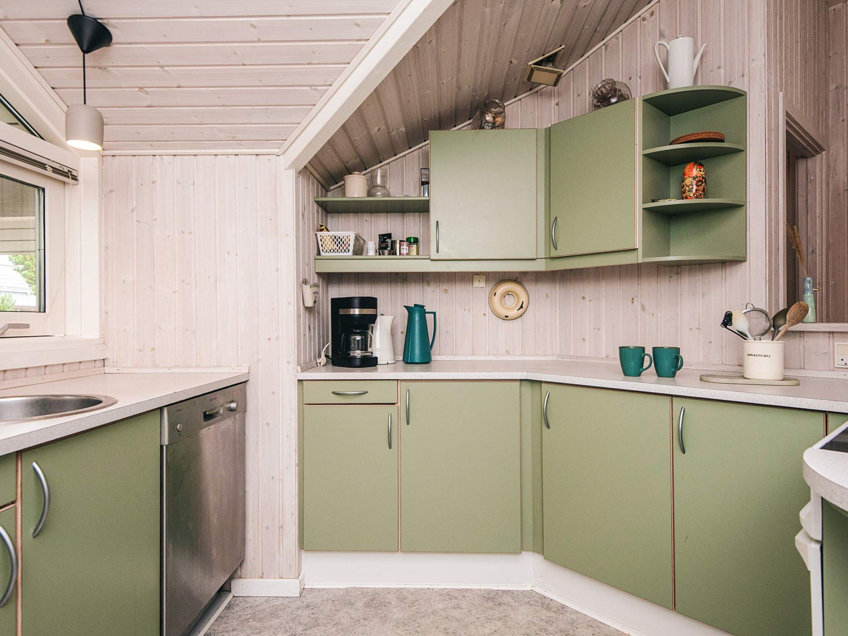 A kitchen with green cabinets, a coffee maker, and a window.