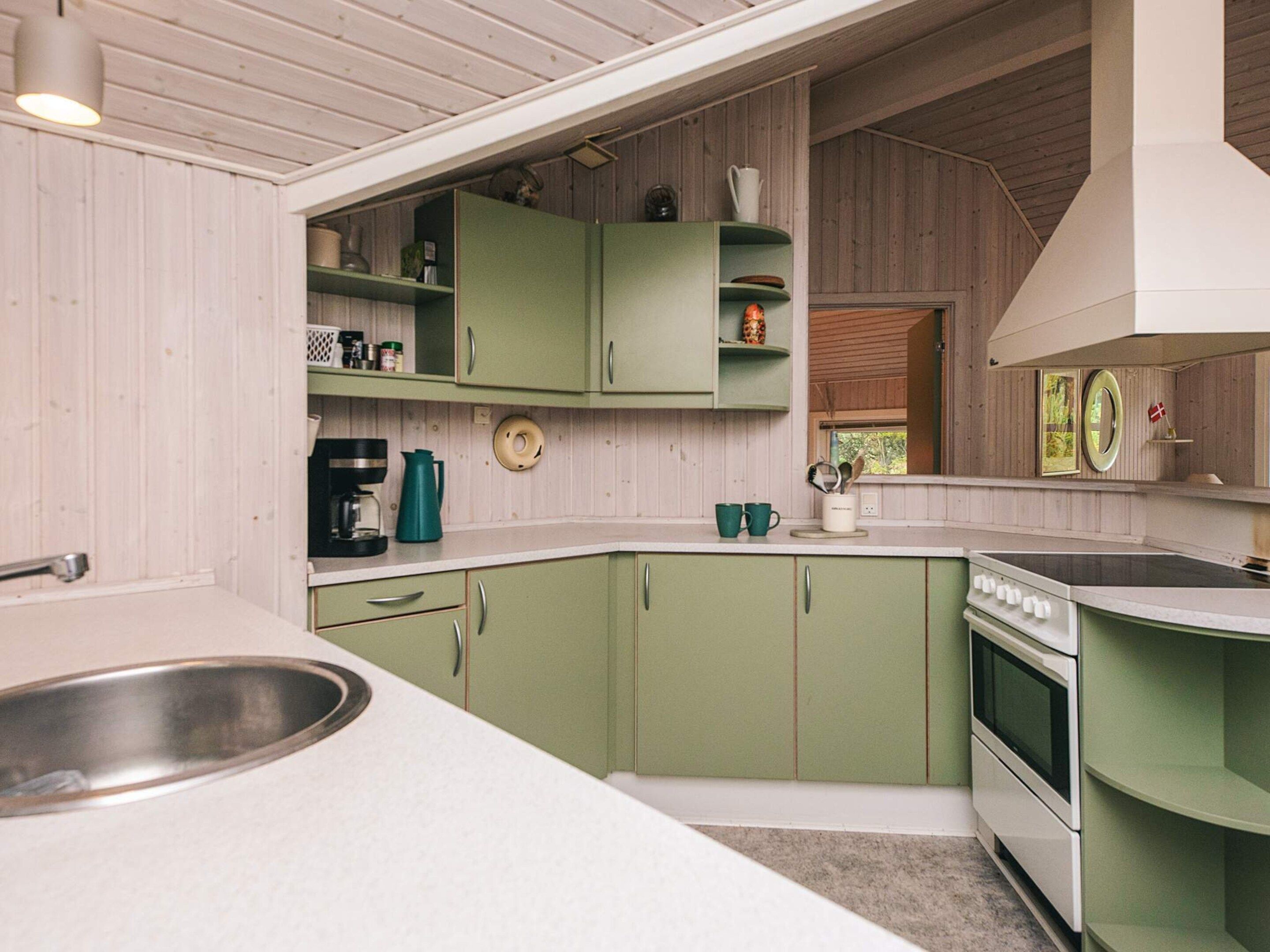 A compact kitchen with green cabinets, a white countertop, a sink, a coffee maker, and a stove.
